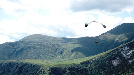 Paraglider flying over mountains during summer day - Georgia, kazbegi
