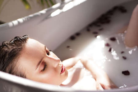 An Attractive girl relaxing in bath with petals on light backgroundの写真素材