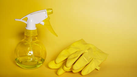 Yellow rubber gloves and a plastic spray bottle for detergent on a yellow backgroundの写真素材
