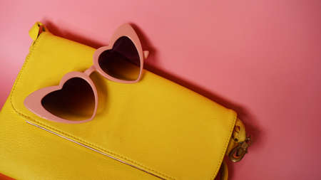 Yellow bag and heart-shaped sunglasses on pink background - summer pictureの写真素材