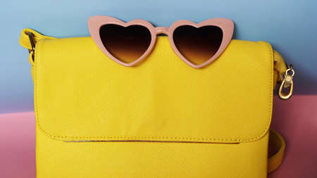Yellow bag and heart-shaped sunglasses on pink and blue background - summer pictureの写真素材