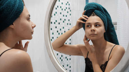 Young woman has problems with skin on the face - She looks in the mirror in the bathroomの写真素材