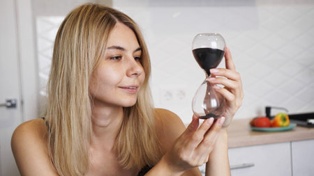 A girl looks at the hourglass and smiles. A woman sits in a bright kitchen and and waits, time...