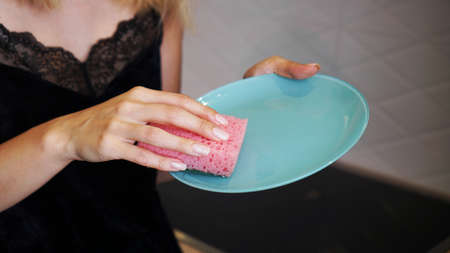 Blue plate with pink dish sponge in hand on blurred kitchen backgroundの写真素材