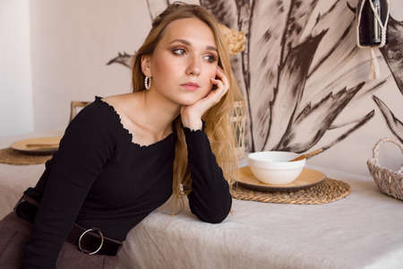 Sad lonely young woman sitting in the kitchen at home. Kitchen in the scandinavian styleの写真素材