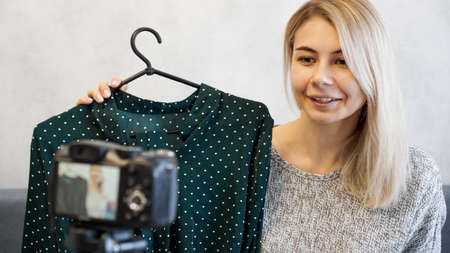 Fashion blogger recording video for blog. Woman in front of the camera holding a green dress in her hands. Close up portraitの写真素材