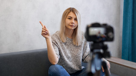Young female blogger talks about business or records a lecture. Woman shows with on a gray wall....