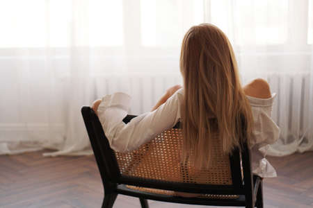Beautiful young woman relaxing, leaning back in chair at home, looking at windowの写真素材