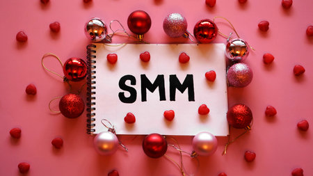 The inscription SMM in a notebook on a pink festive background. Red and pink Christmas balls and...