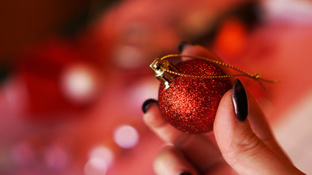 Female hand holds red ball on Christmas background decorated - bokeh lights