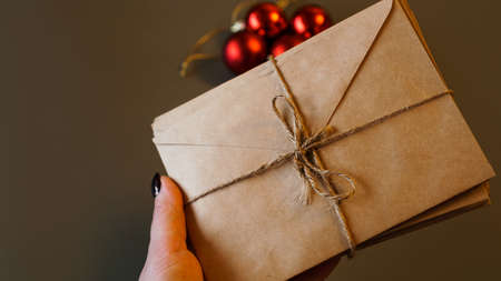 Christmas composition. Craft envelopes and Christmas red balls with copy space. Stack of letters tied with twine in handの写真素材