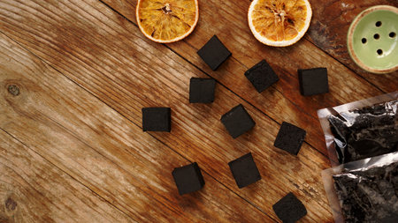 Coals for hookah on wooden background with dry oranges, tobacco and bowl. Place for text