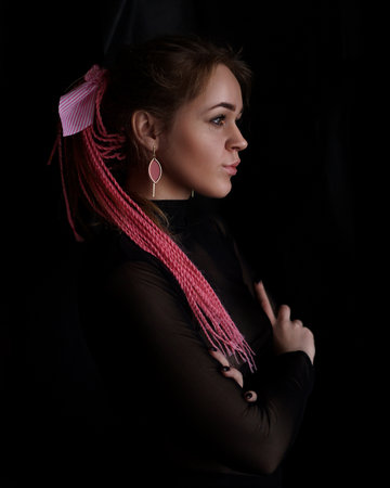 A beautiful girl with pink afro or zizi pigtails on a black background. Portrait with a fashionable high hairstyle and quality retouching with natural skinの写真素材