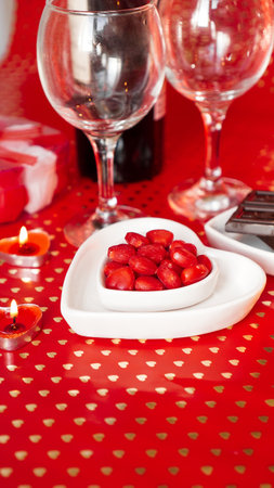 Valentines day. Bottle of vine, glasses, red roses, candles - red background. Love dinner concept - Vertical photoの写真素材