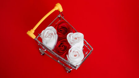 Red and white roses flower on shopping cart on red background. Shopping holiday for valentines day love conceptの写真素材