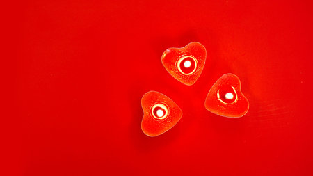 Three red burning candles with heart shaped decorations on red background. St Valentines day.の写真素材