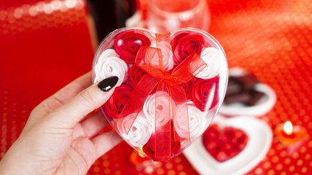 Woman hands holding a gift box in heart shape with beautiful roses over red festive background. Concept of giving a gift on Valentines day holidaysの写真素材