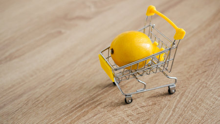 Lemon in a supermarket cart on kitchen table - wooden background. Online shopping concept. Small budget conceptの写真素材