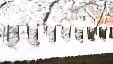 Wooden fence gate covered in white snow at heavy snowing snowstorm, bushes in background. Snow on a wooden fence as background image.の写真素材