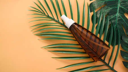 Suntan lotion bottle on soft orange background with tropical leaf. Top view, copy space. Sun protection cosmetic products, summer skin care conceptの写真素材