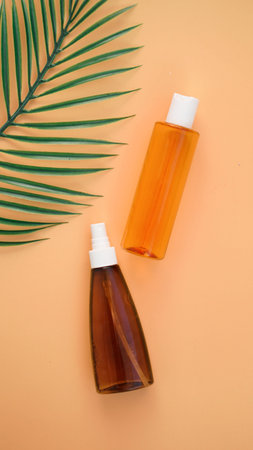 Suntan lotion bottle on soft orange background with tropical leaf. Top view, copy space. Sun...