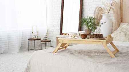 Breakfast set close up in the room. Cups on a tray with vase on the bed. Selective focus. Scandinavian style.の写真素材