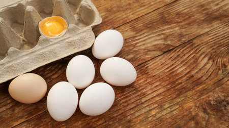 White eggs carton and cracked egg half with yolk top view on wooden background. Easter and healthy food breakfast cooking conceptの写真素材