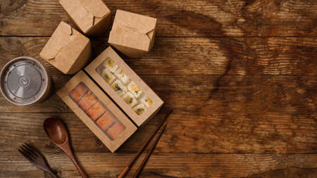 Asian food delivery. Packaging for sushi and woks. Food in paper containers on wooden backgroundの写真素材