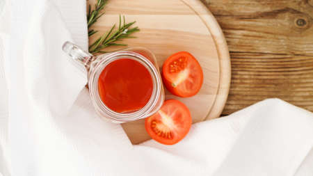 Tomato juice in glass jar, fresh tomatoes and sprigs of rosemary on wooden cutting board and white towel - Top viewの写真素材