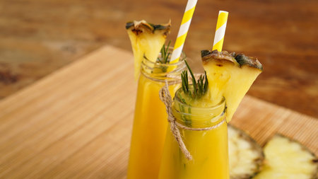 Fresh made Pineapple Juice with Ice in a small glass bottle on wooden background. Homemade drink.