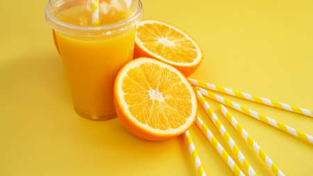 Orange juice in fast food closed cup with tube on yellow background. Sliced orange and yellow paper straws for a drinkの写真素材