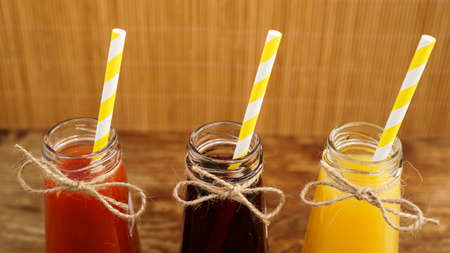 Three multicolored drinks in the bottles on a wooden bamboo background. Bottled paper straws. The bottle is tied with twine. Homemade drinkの写真素材