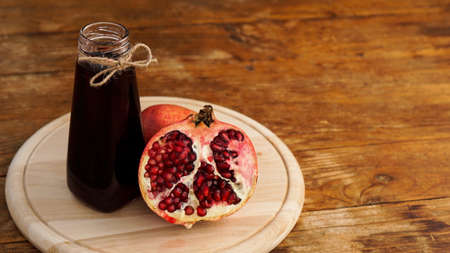 Ripe pomegranates with juice on wooden background. Red juice in small glass bottle on wooden backgroundの写真素材