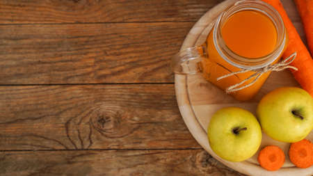 Apple and carrot juice in glass, fresh vegetables and fruits on wooden background. Rustic style. Homemade drink with vitaminsの写真素材