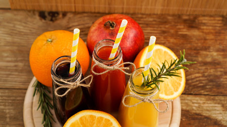 Home made lemonade in little bottles. Multicolored juices and fruits on wooden background. Paper...