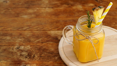 Pineapple juice in a glass jar. Pineapple slices decorate the drink. Juice on wooden background....