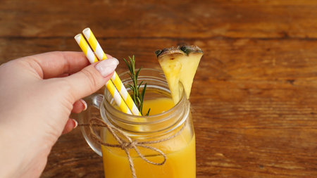Woman Hand holds a straw, a glass of fresh pineapple juice, close up