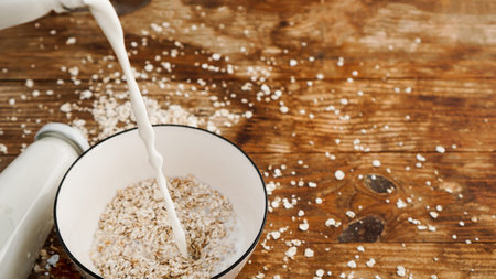 Oatmeal in a bowl. Milk is pouring into a bowl on a wooden background.