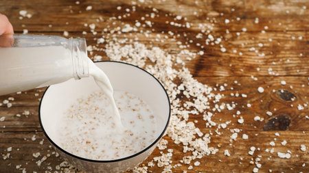 Oatmeal in a bowl. Milk is pouring into a bowl on a wooden background.