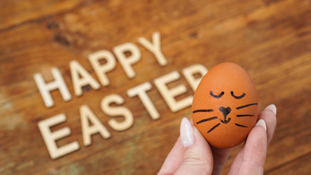 A female hand holds egg with a cute face. Happy Easter concept. Holiday postcardの写真素材