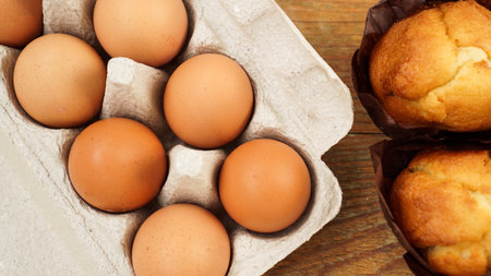 A tray with eggs and fresh tasty muffins in paper forms on a wooden background.