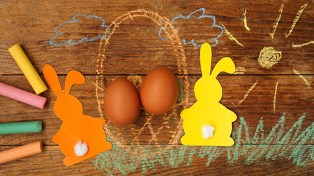 Two Easter bunnies made of paper and eggs in a basket. Drawn with chalk