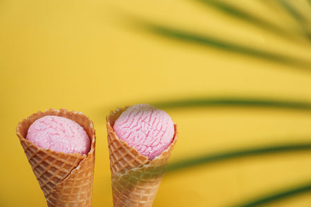 Two strawberry ice creams in a cone on a yellow background. Tropical leaf