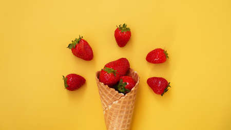 Ice cream cone with strawberries on a yellow background. Red berries in a waffle cone. Summer photoの写真素材