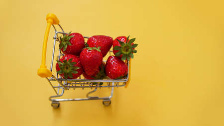 Fresh strawberries in a shopping cart on a bright yellow backgroundの写真素材