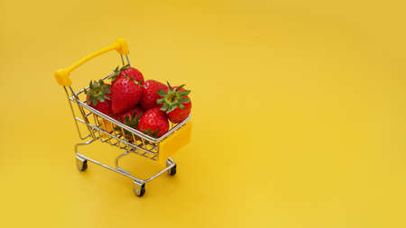 Fresh strawberries in a shopping cart on a bright yellow backgroundの写真素材