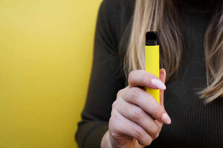 Yellow disposable electronic cigarette in female hand. Bright yellow backgroundの写真素材