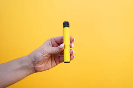 Yellow disposable electronic cigarette in female hand. Bright yellow backgroundの写真素材