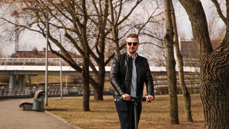 Young man in a black jacket and sunglasses rides an electronic scooterの写真素材