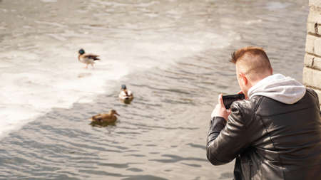 A young man takes pictures of ducks on the water. View from the back.の写真素材